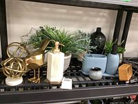 Full shelf view showing gold bird figure, gold sphere sculpture, faux plants, light blue bathroom accessories, and black mosaic vase