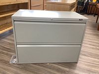 Front view of a light gray 2-drawer metal filing cabinet showing integrated handles and lock front.