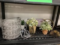 Display of all items on black shelf showing glass bead wall lamp, faux plants, metal sculptures, and bathroom sign