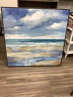 Full view of the framed canvas print showing the seascape artwork with clouds, ocean, and beach in blue and beige tones.
