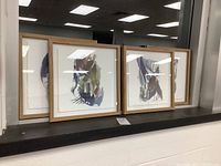 Four framed abstract art prints in wood frames with glass, shown on window ledge.