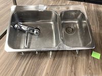 Full view of stainless steel double sink with mounted faucet on wooden floor.