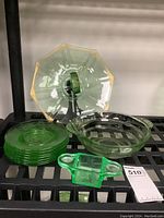 Green Depression glass items on shelf including a pedestal pastry dish, bowl, salt and pepper holder, and stack of plates.