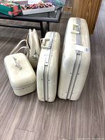 Three cream/ivory vintage hard-sided luggage pieces arranged side by side on wood floor showing sizes and condition