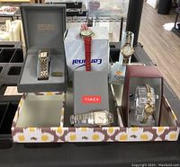 Lot containing five wrist watches displayed on patterned tray, showing watches with metal and leather bands.