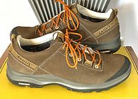 Side angle view of brown leather low cut hiking shoes with orange laces on yellow surface.