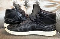 Side profile view of the right and left shoes showing black leather uppers, black laces, white soles, and embossed wing logos on the collars