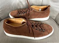 Pair of brown suede Ron White men's sneakers viewed from the outer and inner sides showing the suede material, lace design and white soles.