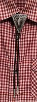 Front view of vintage bolo tie worn on a red and white checked shirt, showing the triangular metal slide with a central black stone and detailed engravings.