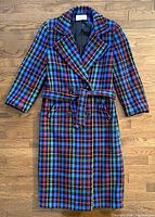 Full front view of the ladies long colorful plaid wool coat laid flat on wood floor.