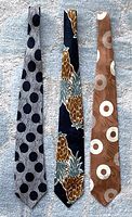 Three full-length ties laid flat on a light carpet: grey polka dots, black pineapple pattern, and brown circular design.