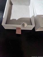 Front photo of the sterling silver ring with sun design resting inside an open box with light brown velvety interior.