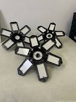 Three black LED garage lights with foldable panels arranged on a table showing five rectangular LED arrays each.