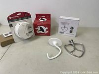 Lot contents including stainless steel flat beater, dough hook, ceramic heater bulb in box, and 2-in-1 smoke & carbon monoxide alarm in original packaging