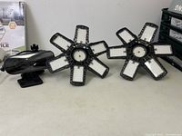 Two black multi-panel LED lights and one rectangular motion sensor light on a white surface.