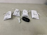 The Moskitto Pro watch alongside four white drawstring carry bags labeled Moskitto Pro and a USB cable arranged on a flat surface.