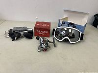 Overview of all three items showing ski goggles, fishing reel with Quantum Optix box, and black sunglasses