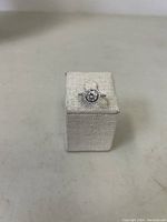 Front view of sterling silver size 6 ring with round center stone and halo of smaller stones on a display stand.