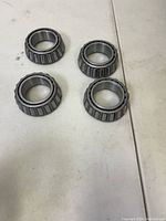 Four Timken 25580 tapered roller axle bearings arranged on a white surface for display.