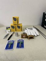 Various items on a table including yellow Synoshi drill bit boxes, white work gloves, wooden blocks with bits, metal socket piece, Graco switch tips, and a metal rod.