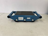 Blue steel machinery skate with rubber top and 6 nylon rollers, shown from front side against white background.