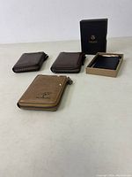 Four wallets placed on a white table, three brown Aiks Kangaroo wallets with zipper and one black Vulkit wallet in original box.