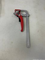 Full view of the Craftwood clamp showing metal bar and red trigger handle lying on flat white surface