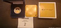 Photo of the proof dollar coin in its velvet display case, the commemorative certificate card, and the original yellow and white presentation box.