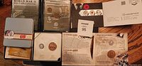Photo showing multiple coin sets including the World War II Five Cents Collection in a folder, 60th VE Day Anniversary boxed sets, and accompanying documentation and packaging.