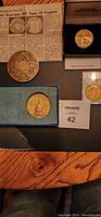 Photo showing four commemorative medallions including a large detailed calendar medal, Nevada Bicentennial medallion in box, smaller gold medallion in protective case, and bronze coin depicting US Capitol in blue case, plus newspaper clipping describing bicentennial commemoratives.