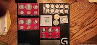 Overview of multiple US Proof Sets in original casing and several individual vintage coins laid out on a table.