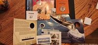 Photo showing the Expo 67 medallion in orange booklet, Titanic commemorative coins, stamps, Titanic ship and iceberg cardboard display, and six string nations item.