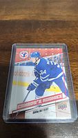 Front image of Auston Matthews rookie hockey card in protective sleeve showing player in Toronto Maple Leafs uniform, card design and branding.