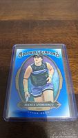 Upper Deck Goodwin Champions tennis trading card featuring Bianca Andreescu with a blue and gold design placed in a plastic protector on a wooden surface.