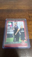 Photo of the Christine Sinclair soccer trading card in a clear protective plastic case on a wood surface.