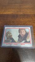 Image of a Star Wars trading card featuring Han Solo and C-3PO in a plastic sleeve placed on a wooden surface.