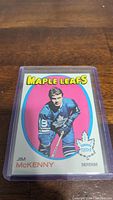 Photo shows a Jim McKenny O-Pee-Chee hockey card in a protective plastic case with colorful pink background and Maple Leafs logo.