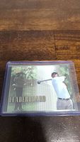 Photo of a Tiger Woods golf card titled 'Leaderboard', showcasing a golfing action image of Tiger Woods. Card is secured in a clear plastic protective case.