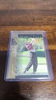 Photo of a Tiger Woods rookie sports card in a plastic sleeve laying on a wooden surface.