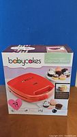 Box front showing the Babycakes Cupcake Maker with product image and branding.
