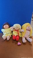 Front view of three Cabbage Patch Kids dolls sitting side by side showing outfits and faces.