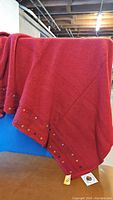 Red knit throw blanket draped showing texture and colorful embroidered edge.