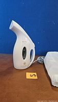 Full side view of white Joy My Little Steamer Go Mini travel fabric steamer with water window and visible power cord, placed on wood surface