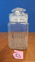 Front view of clear glass jar with lid, showing diamond pattern and knobbed lid.