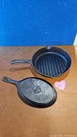 Photo showing both cast iron pieces: 12-inch round grill pan and 7-inch oval skillet with Lodge branding, on flat surface.