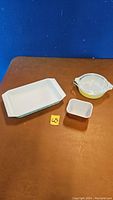 Three items on table: rectangular blue Pyrex butter dish, round yellow Pyrex casserole with lid, small brown and white ceramic dish.