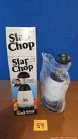 Photo of the Slap Chop small chopper in its plastic wrapping next to its original box with branding and image of the product.