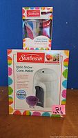 Front view of Sunbeam Igloo Snow Cone Maker box with snow cone cups and straws, showing branding and packaging