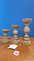 Set of three wooden pillar candlesticks of varying heights, displayed against a blue background.