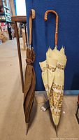 Full view of two closed umbrellas side by side, one brown and one cream floral pattern, both with wooden handles.